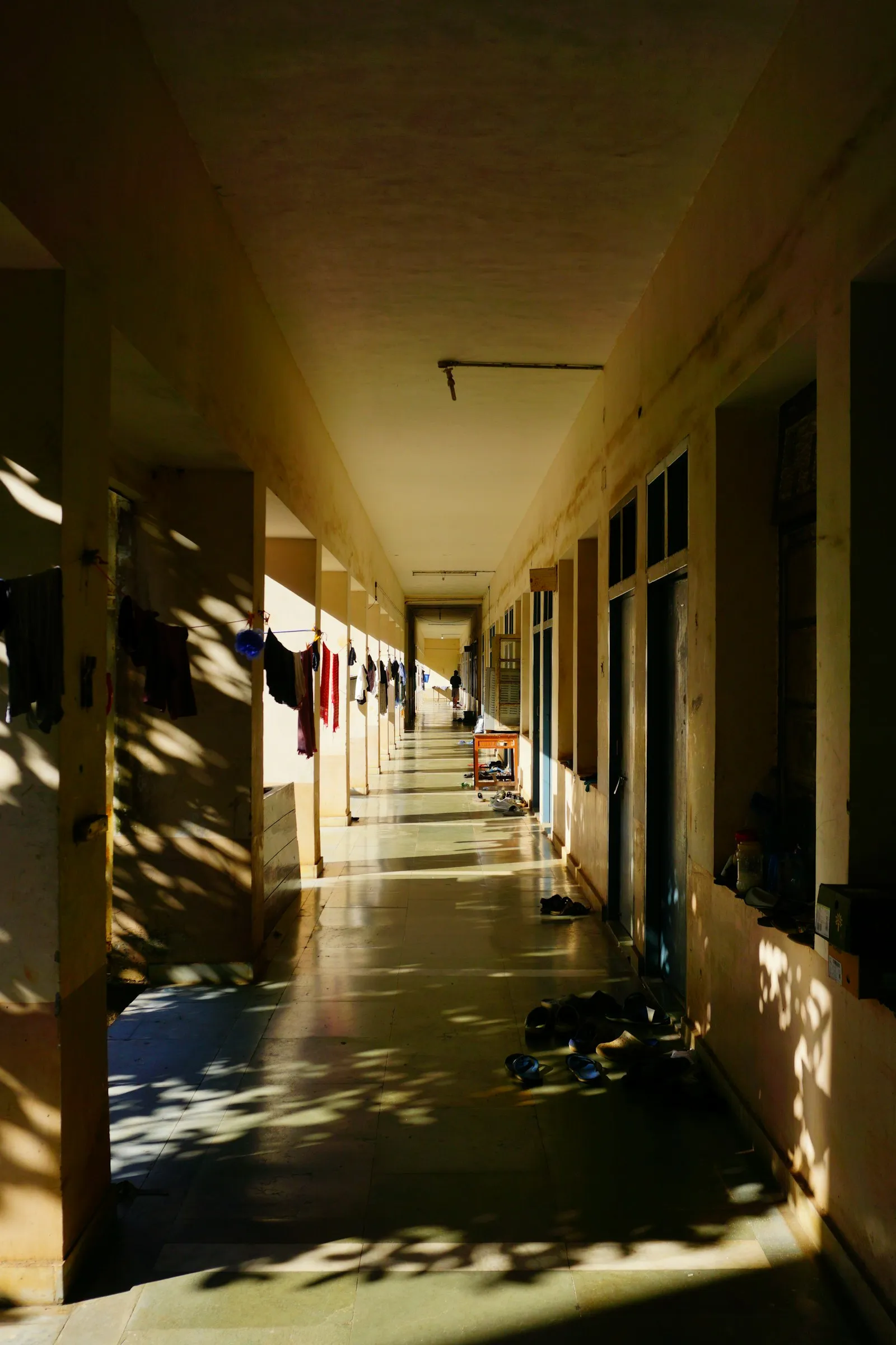 An open-air hostel corridor in afternoon light, with laundry drying outside the rooms
